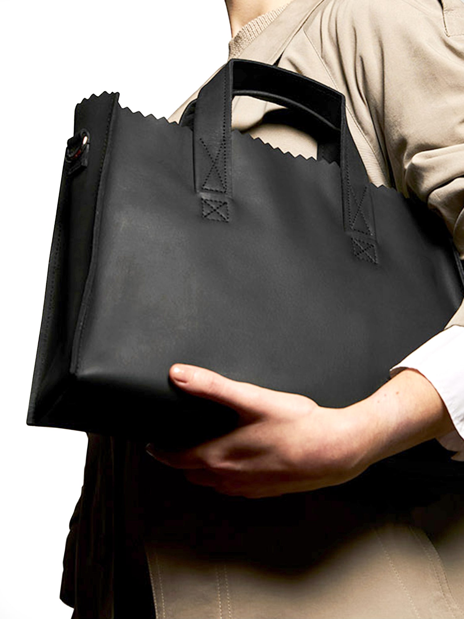 Person holding a black leather bag against a neutral background